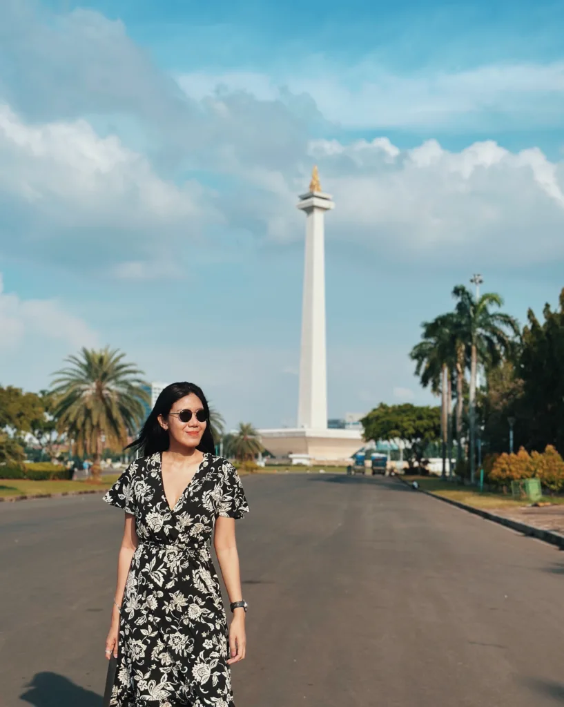 a woman standing on a road with a tall white tower in the background Things to Do in Jakarta